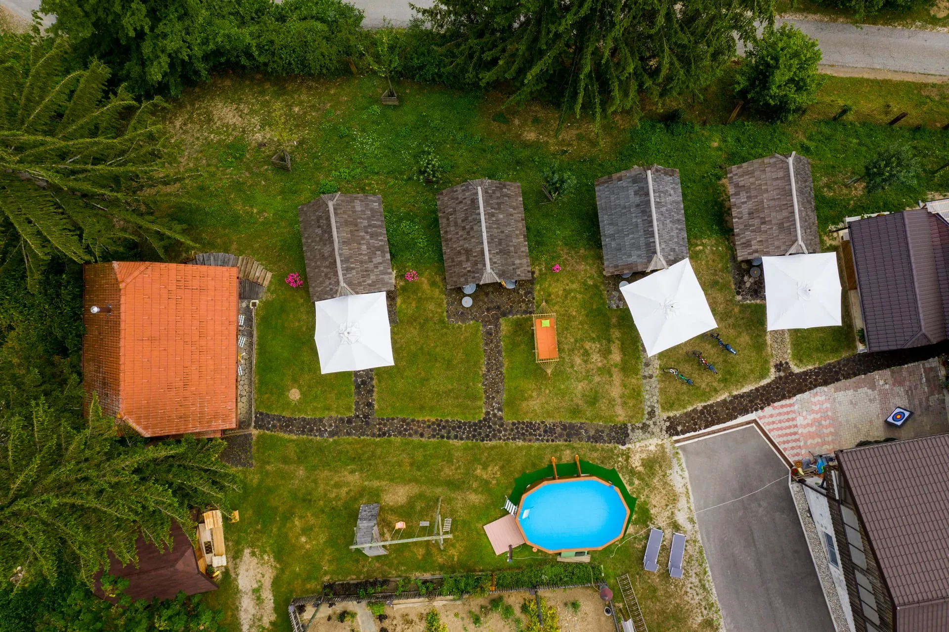 Aerial view of the glamping village — four wooden cabins in a row, a small pool, hammock, and surrounding trees.
