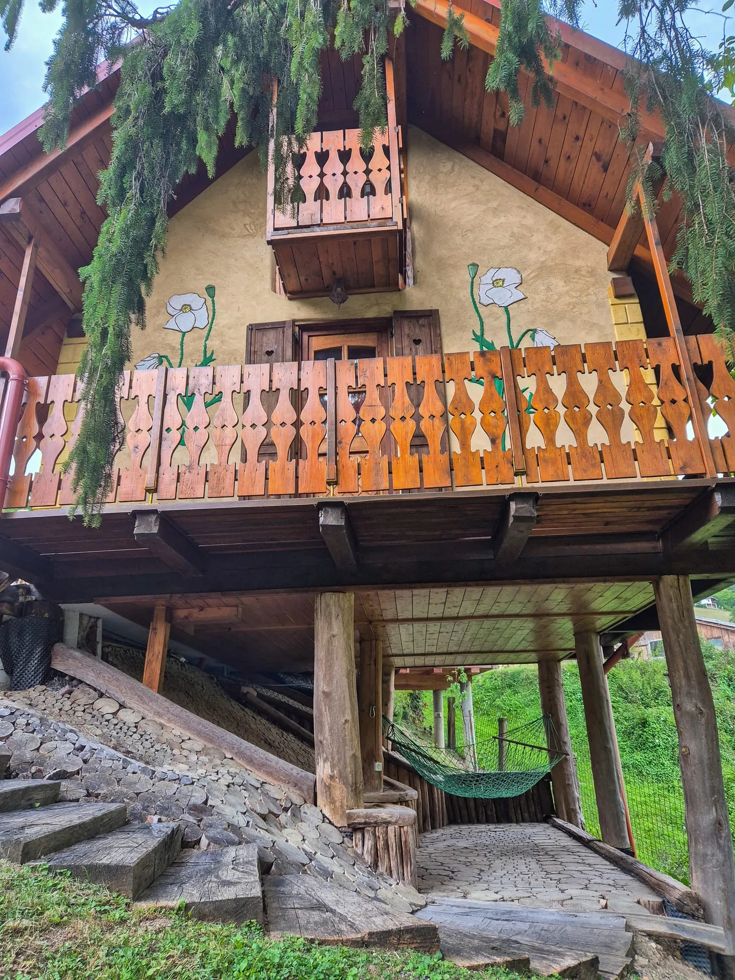 Looking up at the Pastirski stan's wooden balcony from below, evergreen branches overhanging.